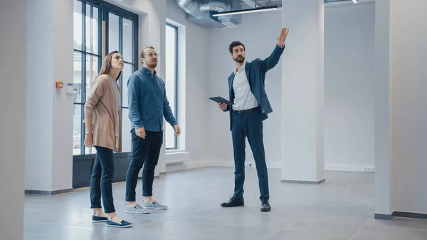Real Estate Agent Showing a New Empty Office Space to Young Male and Female Hipsters. Entrepreneurs Meet the Broker with a Tablet and Discuss the Facility They Wish to Purchase or Rent. — Stock Photo, Image