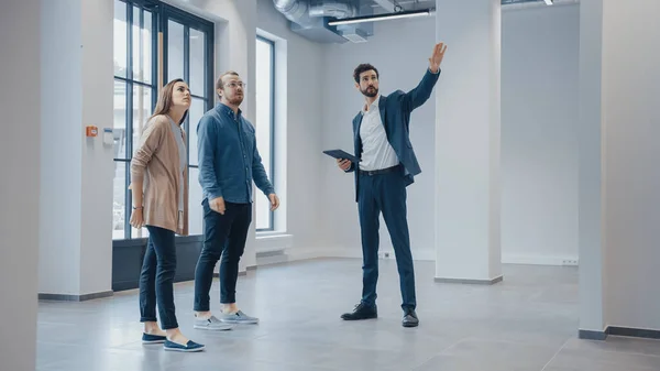 Makelaar toont een nieuwe lege kantoorruimte aan jonge mannelijke en vrouwelijke hippies. Ondernemers Ontmoet de makelaar met een tablet en bespreek de faciliteit die ze willen kopen of huren. — Stockfoto