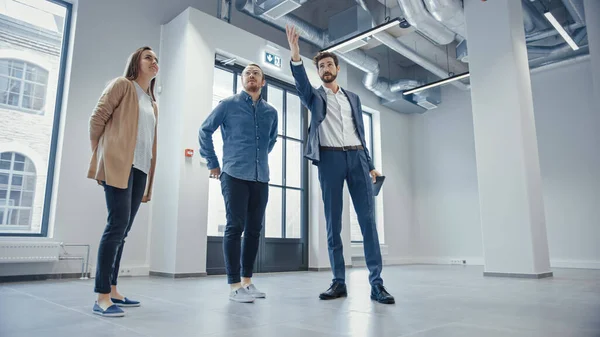 Makelaar toont een nieuwe lege kantoorruimte aan jonge mannelijke en vrouwelijke hippies. Ondernemers Ontmoet de makelaar met een tablet en bespreek de faciliteit die ze willen kopen of huren. — Stockfoto