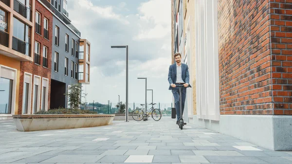 Ung affärsman i kostym rider för att arbeta på en elektrisk skoter. Modern entreprenör använder samtida ekologiska transporter för att gå på ett kontorsmöte. — Stockfoto