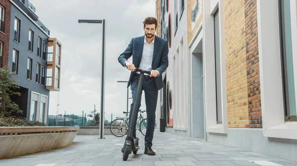 Jovem empresário em um terno começa a montar em um Scooter elétrico. Empreendedor moderno usa transporte ecológico contemporâneo para ir em uma reunião de escritório . — Fotografia de Stock