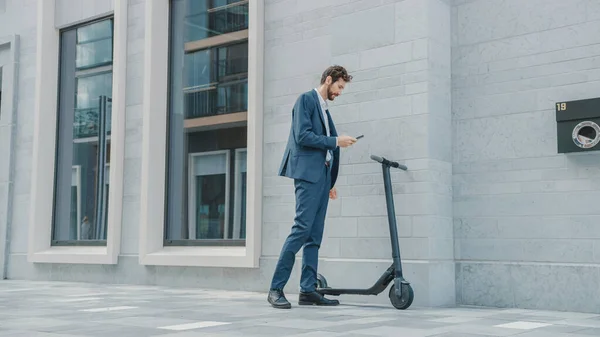 Επιχειρηματίας σε ένα κοστούμι ενεργοποιεί ένα ηλεκτρικό σκούτερ με ένα Smartphone. Σαρώνει τον κώδικα QR. Σύγχρονη Επιχειρηματίας Χρησιμοποιεί Σύγχρονη Οικολογικές Μεταφορές για να πάει σε μια συνάντηση του γραφείου. — Φωτογραφία Αρχείου