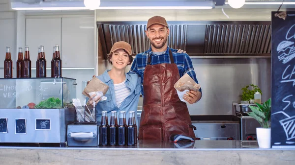 Employees masculinos e femininos bem sucedidos do caminhão do alimento pose para a câmera. Usam Caps Castanhos. Eles são alegres e sorridentes. Caminhão comercial ou quiosque que vende comida de rua e bebidas . — Fotografia de Stock
