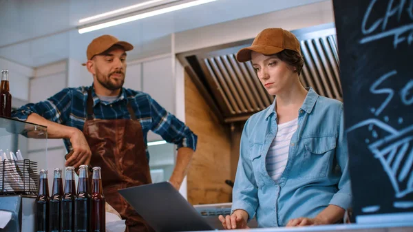 Dipendenti di successo Food Truck in berretti marroni. La femmina sta usando il computer portatile nel loro camion commerciale o chiosco che vende Street Food e bevande. — Foto Stock