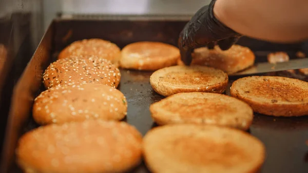 Ízletes feles egy Cook Flipping Burger zsemle szezámmaggal egy forró gázra vagy elektromos grillezőre. Friss ínyenc hamburgerek készülnek. — Stock Fotó