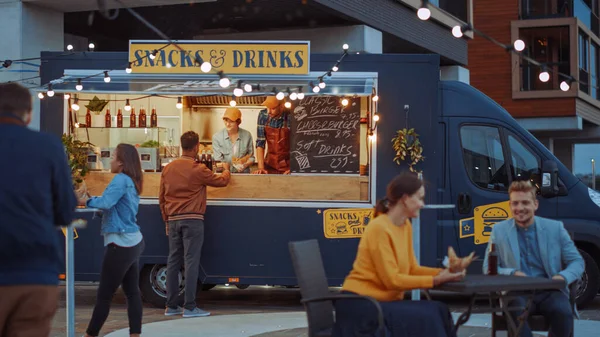 Food Truck Employee Hands Out a Card Card Terminal For Contactless Payment to Young Hipster Customer, who is Buying a Tasty Burger. Commercial Truck Selling Street Food in Modern Cool Neighbourhood.