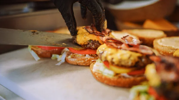 Savoureux plan rapproché d'un cuisinier préparant des hamburgers. Food Chef ajoute de la soupe au-dessus des pains aux graines de sésame. Des hamburgers gastronomiques frais avec galette de boeuf, salade, tomate et concombre sont en préparation. — Photo