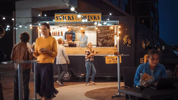 Food Truck Employee Hands Out Beef Burgers, Fries and Cold Drinks to Happy Hipster Customers (dalam bahasa Inggris). Orang-orang makan di meja luar. (Inggris) Commercial Truck Selling Street Food in a Modern Place Near the Sea. — Stok Foto