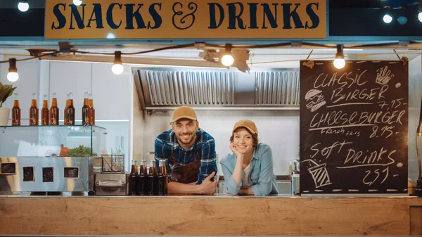 Les employés masculins et féminins de camion de nourriture avec succès posent pour l'appareil photo. Ils portent des casquettes brunes. Ils sont joyeux et souriants. Camion commercial ou kiosque vendant de la nourriture et des boissons de rue. — Photo