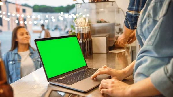 Computador portátil com tela verde Mock Up Screen é colocado em um contador em um caminhão de comida de rua ou quiosque que vende hambúrgueres e bebidas. Clientes felizes recebem suas ordens . — Fotografia de Stock