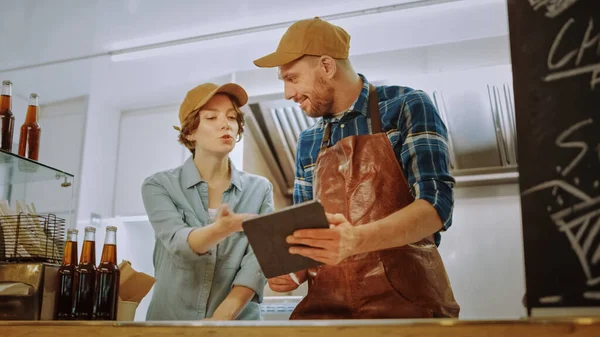 Succesvolle Food Truck Man en Vrouw Werknemers in Brown Caps gebruiken een Tablet Computer. Zij bespreken hun winst- en toekomstplannen. Commerciële Truck of Kiosk verkoopt Street Food and Drinks. — Stockfoto