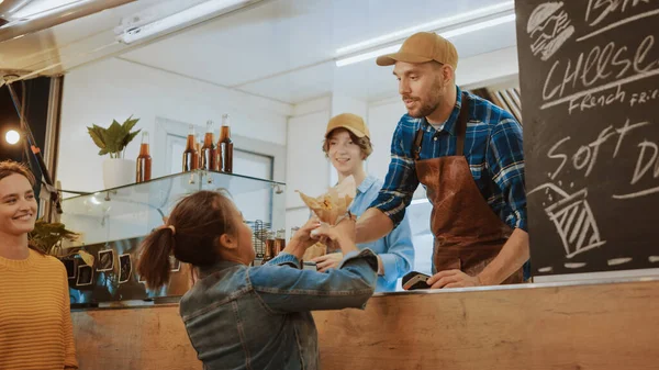 餐车员工向一位快乐的年轻女性分发新制造的汉堡。年轻的女士正在用不可接触的信用卡购买食物。现代平房街坊的街头食品卡车销售汉堡 — 图库照片