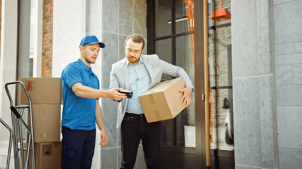 Delivery Man Postacsomagot ad egy üzleti ügyfélnek, aki aláírja az elektronikus aláírás POD eszközt. A Stílusos Modern Városi Office Area Courier szállít kartondoboz csomag egy ember. — Stock Fotó