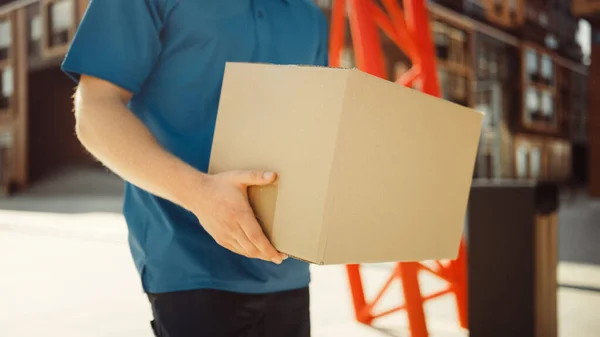 Entrega El hombre sostiene el paquete de la caja de cartón camina a través del distrito de negocios moderno y elegante. Mensajero en el camino para entregar el paquete postal a un cliente. Enfoque en el paquete . — Foto de Stock