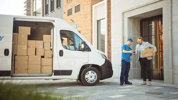 Bezorger geeft postpakket aan een zakelijke klant, die elektronische handtekening POD apparaat tekent. In stijlvolle moderne stedelijke kantooromgeving koerier bezorgt kartonnen doos Pakket aan een man. — Stockfoto