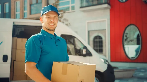 Portret van Handsome Delivery Man houdt Kartonnen doos Pakket Staande in Modern Stijlvol Business District met Delivery Van in de achtergrond. Glimlachende koerier op weg naar postpakket leveren aan de klant — Stockfoto