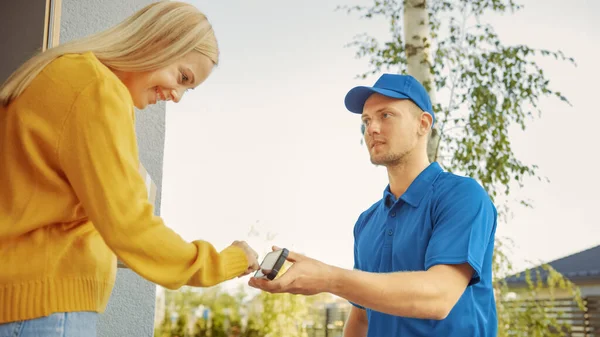 Beautiful Young Woman Meets Delivery Man who Gives Her Cardboard Box Package, She Signs Electronic Signature POD Device. 교외 이웃에 있는 프로 셀 을 부드럽게 배달하라 — 스톡 사진