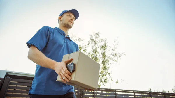 Tiro de ángulo bajo del hombre joven hermoso de la entrega que entrega el paquete de la caja de cartón. Mensajero entregando paquete en el barrio de los suburbios . — Foto de Stock