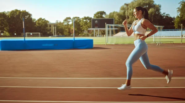 Девушка в светло-синем спортивном топе и бегает по стадиону. Она бежит теплым летним днем. Спортсмен делает свою рутинную спортивную практику на треке . — стоковое фото