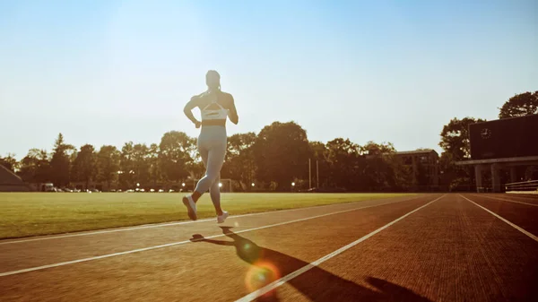 Vacker Fitness kvinna i ljusblå atletisk topp och leggings Jogging i en stadion. Hon springer på en varm sommareftermiddag. Idrottaren gör sin rutin sport praxis på en bana. Låg vinkel. — Stockfoto