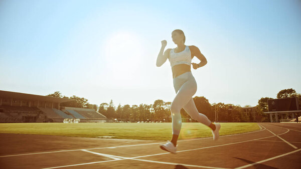 Beautiful Fitness Woman in Light Blue Athletic Top and Leggings Jogging in a Stadium. She is Running on a Warm Summer Afternoon. Athlete Doing Her Routine Sports Practice on a Track. Low Angle.