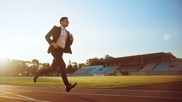 Giovane uomo d'affari serio in giacca e cravatta che corre in uno stadio all'aperto. Porta gli occhiali e tiene in mano un cellulare. Lavoro d'ufficio a caccia di obiettivi. Gestione satira. — Foto Stock