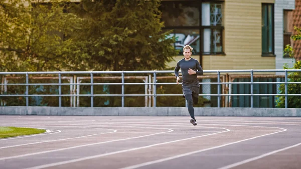 Smiling Athletic Fit Man in camicia grigia e pantaloncini da jogging nello stadio. Sta correndo veloce in un caldo pomeriggio d'estate. Atleta che fa la sua pratica sportiva di routine. — Foto Stock