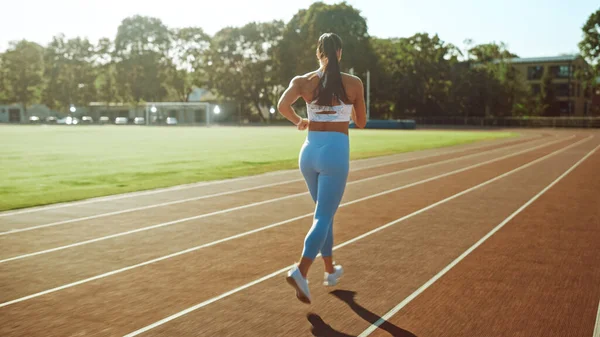 スタジアムでジョギングライトブルーアスレチックトップとレギンスで美しいフィットネスガール。彼女は暖かい夏の午後に走っている。陸上競技の練習をする選手. — ストック写真
