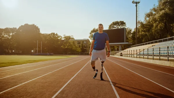 Спортсмен-инвалид с протезными бегущими лезвиями позирует во время тренировки на открытом стадионе в солнечный день. Ампутированный бегун стоит на треке. Спортивный буллит . — стоковое фото