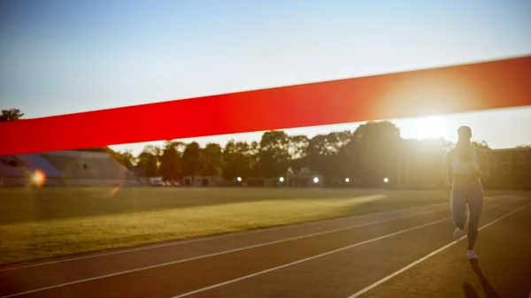 Belle course féminine avant de franchir la ligne d'arrivée sur une arène sportive professionnelle. Femme athlétique en compétition dans un stade. Célébration de la victoire. — Photo