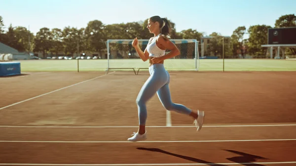 Женщина в светло-синем спортивном топе и бегущая на ногах по стадиону. Она бежит быстро теплым летним днем. Спортсмен делает свою рутинную спортивную практику . — стоковое фото