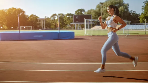 Belle femme de fitness en haut athlétique bleu clair et leggings Jogging dans le stade. Elle court vite un après-midi d'été chaud. Athlète faisant sa pratique sportive de routine. — Photo
