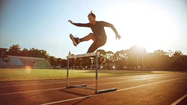Athletic Fit Man in Grey Shirt and Shorts Hurdling in the Stadium. He is Jumping Over Barriers on a Warm Summer Afternoon. Athlete Doing His Routine Sports Practice. — Stock Photo, Image