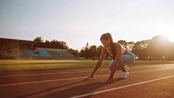 Женщина в светло-синем спортивном топе и легинсах начинает забег на открытом стадионе. Она бежит в теплый летний день. Спортсмен, занимающаяся спортом. — стоковое фото