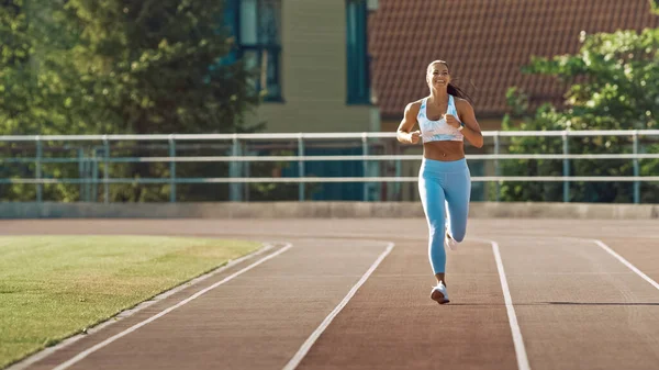 Gyönyörű Fitness nő világoskék Athletic Top és Leggings kocogás a stadionban. Meleg nyári délutánon fut. A sportoló rutin sportedzést tart a pályán.. — Stock Fotó