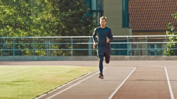 Homme en forme athlétique souriant en chemise grise et chemises Jogging dans le stade. Il court vite un après-midi d'été chaud. Athlète faisant sa pratique sportive de routine. — Photo