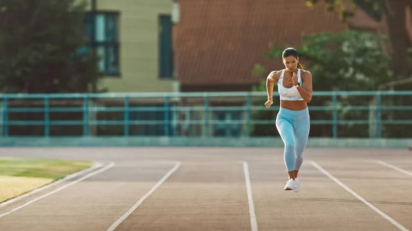 Mulher Fitness bonita em azul claro Atlético Top and Leggings está começando uma corrida de corrida de corrida em um estádio ao ar livre. Ela está correndo em um dia quente de verão. Atleta fazendo sua prática esportiva. — Fotografia de Stock