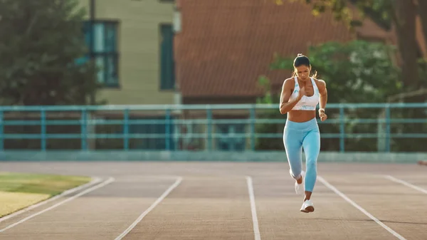 Mulher Fitness bonita em azul claro Atlético Top and Leggings está começando uma corrida de corrida de corrida em um estádio ao ar livre. Ela está correndo em um dia quente de verão. Atleta fazendo sua prática esportiva. — Fotografia de Stock