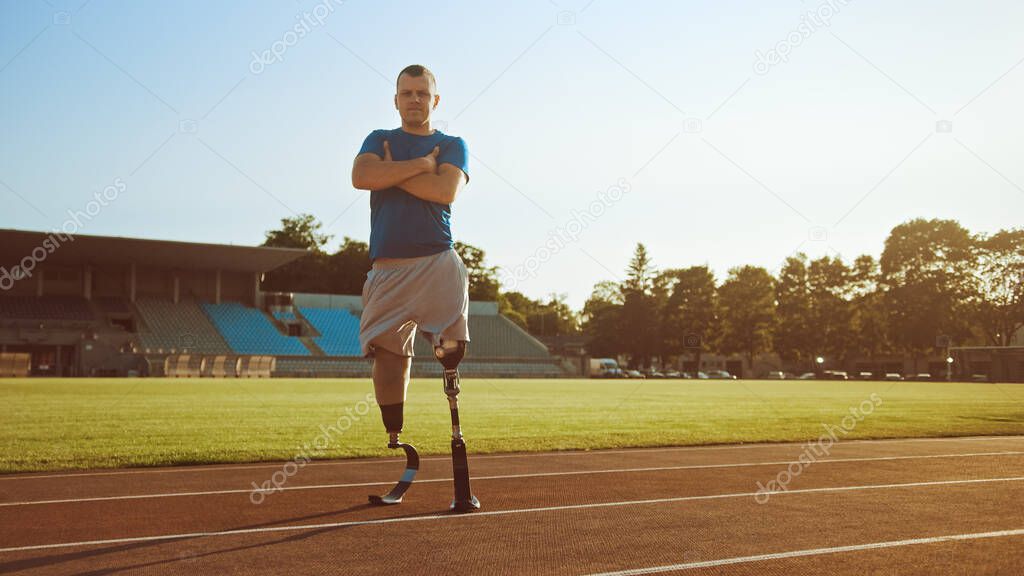 Athletic Disabled Fit Man with Prosthetic Running Blades is Posing with Crossed Arms on an Outdoor Stadium on a Sunny Afternoon. Amputee Runner Standing on a Track. Motivational Sports Shot.