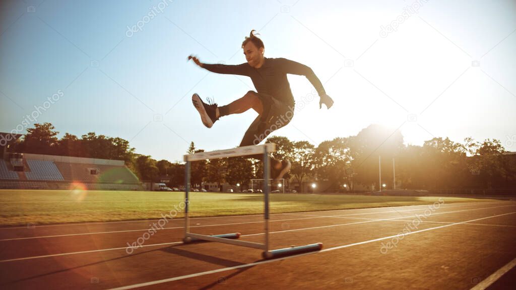 Athletic Fit Man in Grey Shirt and Shorts Hurdling in the Stadium. He is Jumping Over Barriers on a Warm Summer Afternoon. Athlete Doing His Routine Sports Practice.