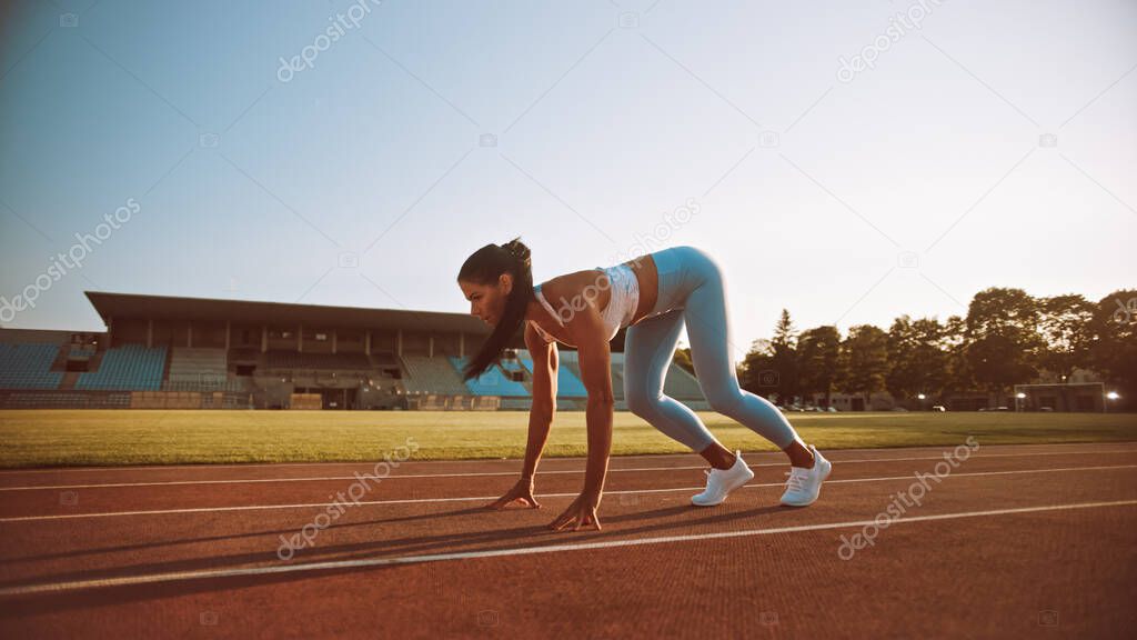 Beautiful Fitness Woman in Light Blue Athletic Top and Leggings is Starting a Sprint Run in an Outdoor Stadium. She is Running on a Warm Summer Day. Athlete Doing Her Sports Practice.