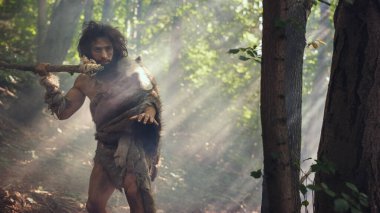 Tarih öncesi ormanda Hayvan Derisi Giyen İlkel Mağara Adamı 'nın Portresi ve Taş Ucu Mızrakla Kürk Avı. Tarih öncesi Neandertal Avcısı Ormanda İlkel Aletlerle Çöpleri Arıyor