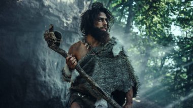 Hayvan Derisi Tutacağı Taşı Giyen İlkel Mağara Adamı Mağaradan çıkıyor ve Tarih Öncesi Araziye Bakıyor, Hayvan Avlamaya Hazır. Neanderthal Ormanda Avlanmaya Gidiyor