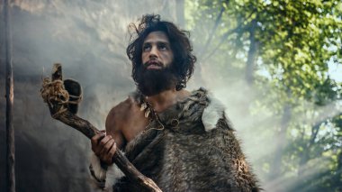 Hayvan Derisi Tutacağı Taşı Giyen İlkel Mağara Adamı Mağaradan çıkıyor ve Tarih Öncesi Araziye Bakıyor, Hayvan Avlamaya Hazır. Neanderthal Ormanda Avlanmaya Gidiyor
