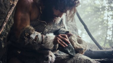 Hayvan derisi giyen ilkel mağara adamı keskin taşla kayaya çarpar ve hayvan avlamak için ilkel araç yapar. İlk Çark 'ı yaratmak için el baltası kullanan Neandertal.
