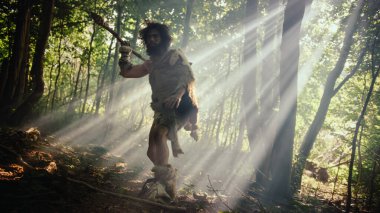 Tarih öncesi ormanda Hayvan Derisi Giyen İlkel Mağara Adamı 'nın Portresi ve Taş Ucu Mızrakla Kürk Avı. İlkel Neandertal Avcısı Ormana Mızrak Atmaya Hazır