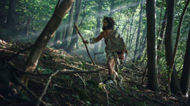 Hayvan Derisi Tutucu Taştan Mızraklı İlkel Mağara Adamı Etrafa Bakınıyor, Hayvan Avı Avında Tarih Öncesi Ormanı keşfediyor. Neanderthal Ormanda Avlanmaya Gidiyor