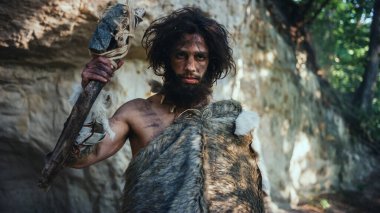 Hayvan derisi tutan ilkel mağara adamı portresi uçlu çekiç. Tarih öncesi Neandertal Avcı Pozisyonu Ormanda İlkel Avcılık. Kameraya Bakma
