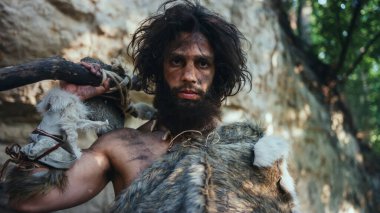 Hayvan derisi tutan ilkel mağara adamı portresi uçlu çekiç. Tarih öncesi Neandertal Avcı Pozisyonu Ormanda İlkel Avcılık. Kameraya Bakma