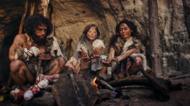 Tarih öncesi avcı-toplayıcı kabilesi Hayvan Derisi Giyen Gece Bir Mağarada Yaşıyor. Neanderthal ya da Homo Sapiens Ailesi Şenlik Ateşi 'nde Isınmaya Çalışıyor, Ateşin Üzerinde Elele tutuşuyor, Yemek Pişiriyor
